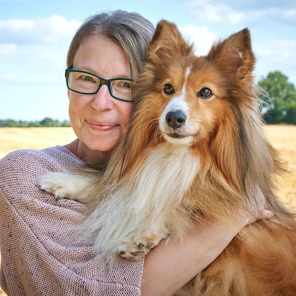 Frau mit Brille hält ihren Sheltie im Arm