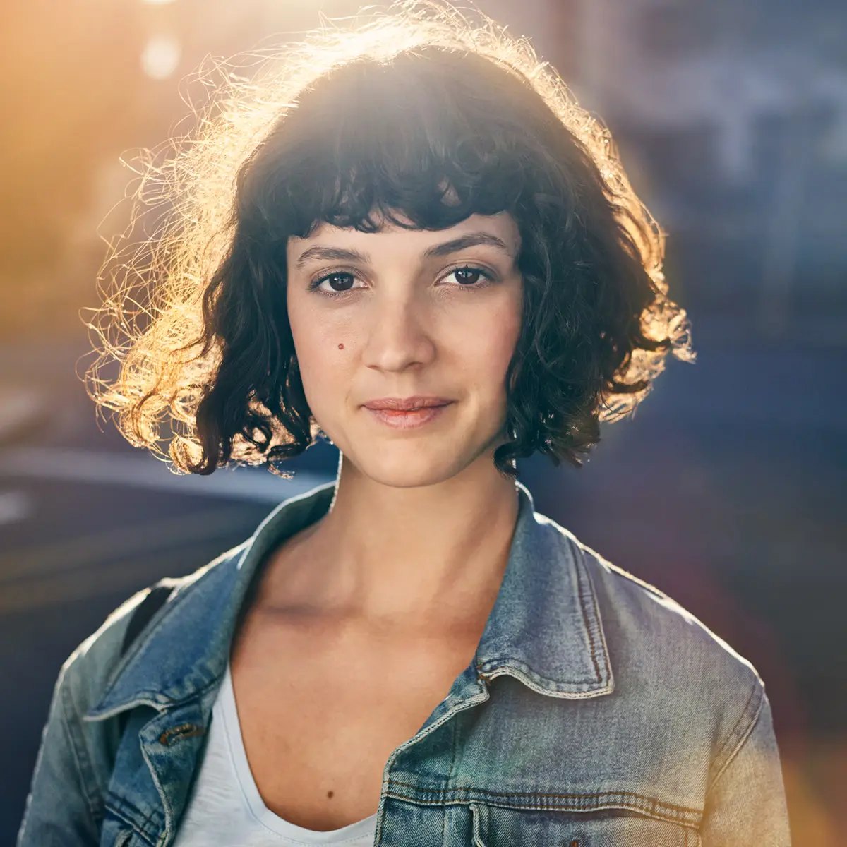 Portrait einer jungen Frau mit Locken im Gegenlicht in der Stadt