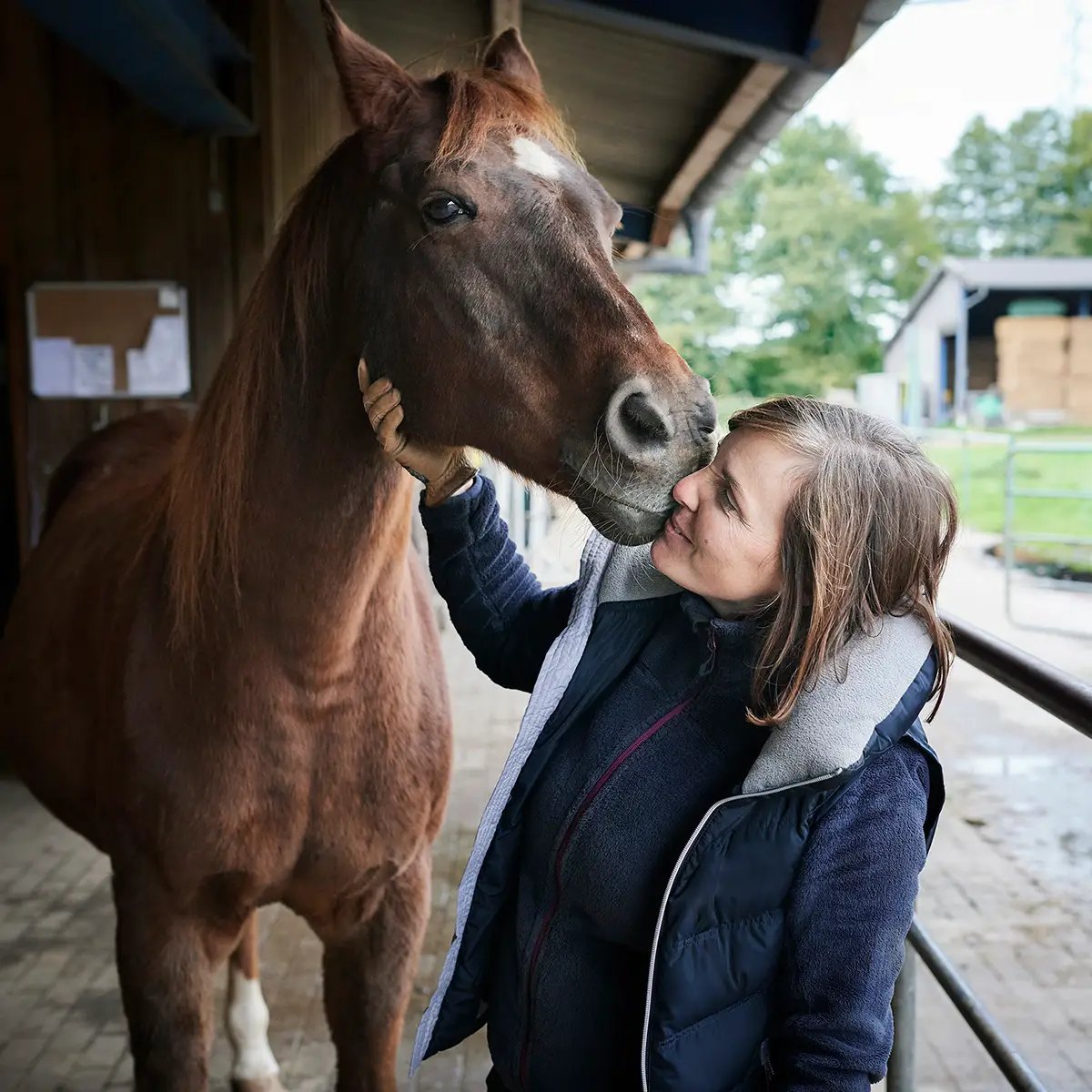 Frau schmiegt sich an ihr Pferd im Stall