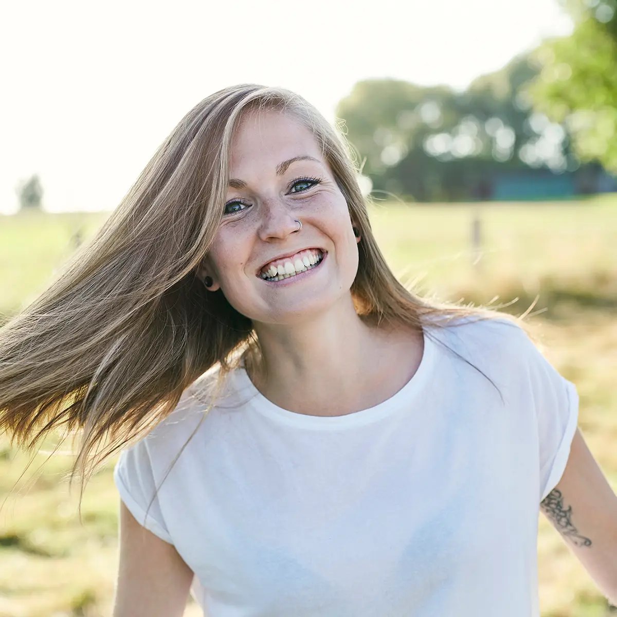 Frau mit wehenden Haaren lacht auf einer Wiese