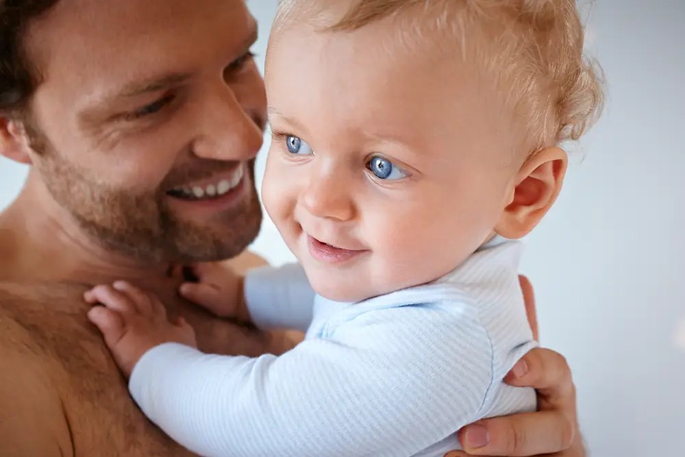 Vater hält sein Baby im Arm, beide lachen
