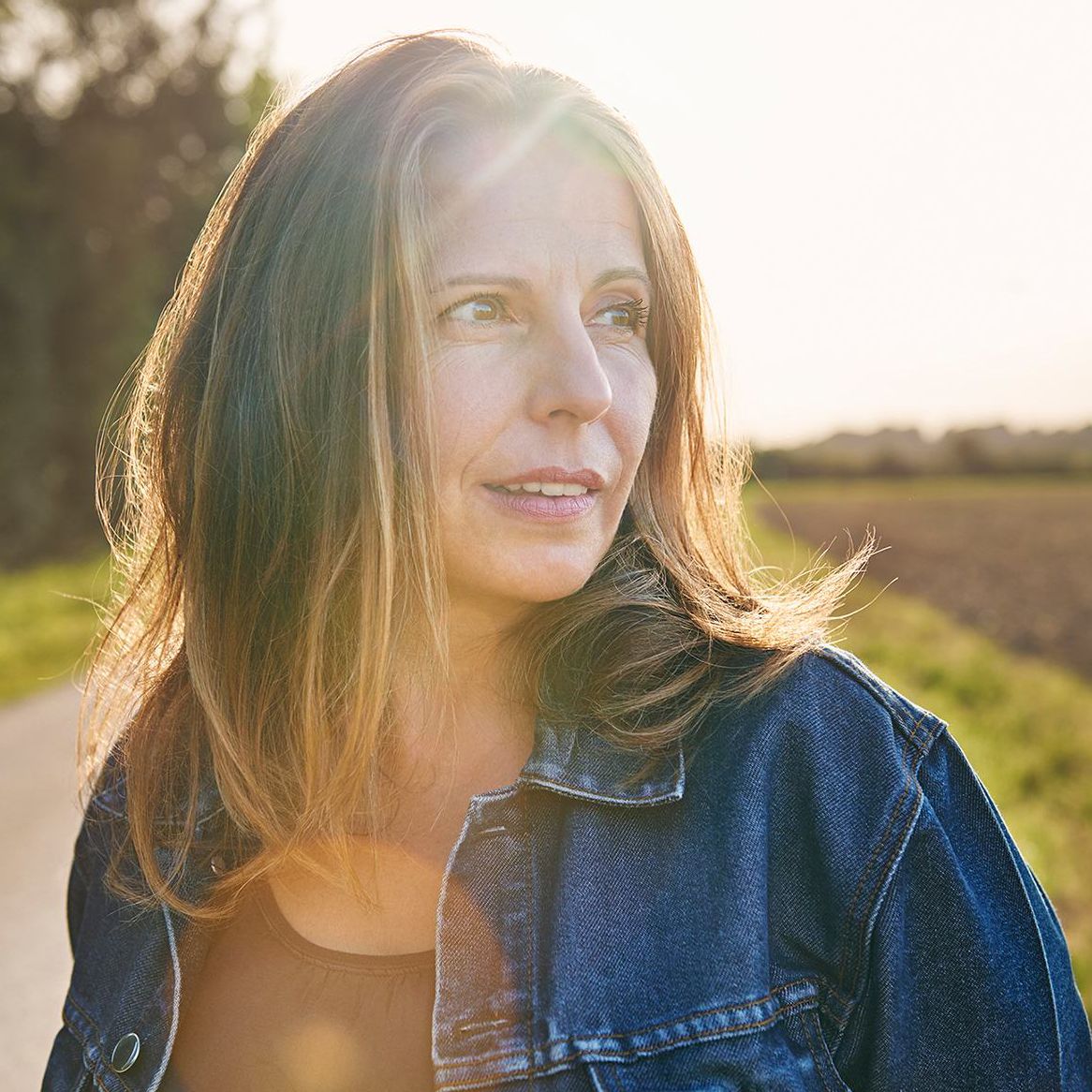 Frau in Jeansjacke im Gegenlicht am Feldrand